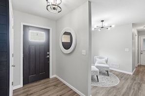 A hallway with a dark door, a round mirror, a ceiling fan, and a patterned rug. - LUXURY COUNTRY RETREAT ~ HEATED POOL, PICKLEBALL COURT, FIRE PIT & COUNTRY VIEWS (Wauseon)