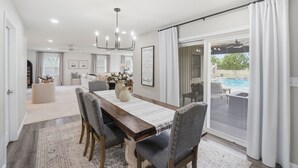 A dining area with a wooden table, grey upholstered chairs, and a view of a swimming pool through a glass door. - LUXURY COUNTRY RETREAT ~ HEATED POOL, PICKLEBALL COURT, FIRE PIT & COUNTRY VIEWS (Wauseon)