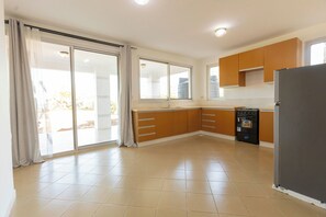A kitchen with a refrigerator, oven, and sliding glass doors leading to a balcony. - Serenity Shores (Dar es Salaam)