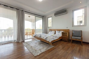 A bedroom with a bed, a chair, a balcony, and a large window. - Serenity Shores (Dar es Salaam)