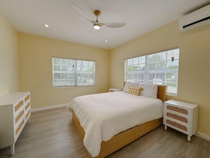 Quarto com cama, mesas de cabeceira, ventoinha no teto e janelas.