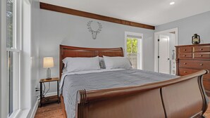 Un dormitorio con una cama de madera, una mesita de noche, una lámpara, un aparador y una decoración de cabeza de venado montada en la pared.