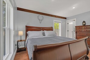 A bedroom with a wooden bed, a nightstand, a lamp, a dresser, and a wall-mounted deer head decoration. - Carriage House In Higganum Center (Haddam)