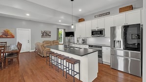 Una cocina moderna con una isla central, electrodomésticos de acero inoxidable y un comedor con mobiliario de madera.