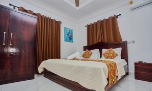 A hotel room with a wooden wardrobe, a bed with a quilted bedspread, two patterned pillows, and a painting on the wall. - 2-bedroom apartment in serene Adenta Municipality with AC (Adenta Municipality)