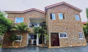 A two-story stone house with a balcony, a front door, and a small porch area. - 2-bedroom apartment in serene Adenta Municipality with AC (Adenta Municipality)