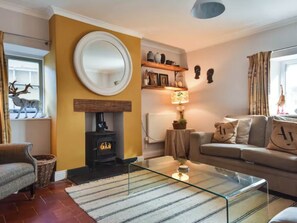 A cozy living room with a fireplace, a sofa, a glass coffee table, and a mirror on the wall. - Acorn Cottage South Cerney, 3 Double Bedrooms in the heart of the village (South Cerney)