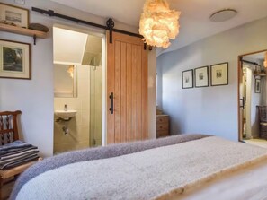 A bedroom with a bed, a wooden wardrobe, a mirror, and a door leading to a bathroom. - Acorn Cottage South Cerney, 3 Double Bedrooms in the heart of the village (South Cerney)