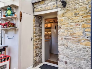 A stone exterior wall, a door leading to a kitchen with a refrigerator, and a small outdoor grill area. - Acorn Cottage South Cerney, 3 Double Bedrooms in the heart of the village (South Cerney)