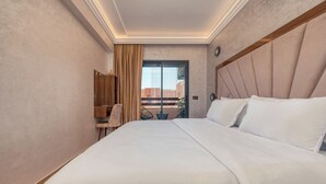 A hotel room with a large bed, a wooden headboard, a desk with a chair, and a view through a glass door. - Luxury Design Apartment in New Residence with Two Pools, Close to All Amenities (Marrakesh)