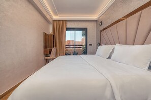 Ein Hotelzimmer mit einem großen Bett, einem hölzernen Kopfteil, einem Schreibtisch mit Stuhl und Blick durch eine Glastür.