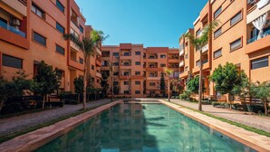 A swimming pool surrounded by multi-story buildings with balconies and air conditioning units. - Luxury Design Apartment in New Residence with Two Pools, Close to All Amenities (Marrakesh)