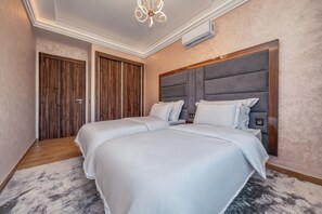 Ein Hotelzimmer mit zwei Betten, einem Holzschrank, einem grauen Kopfteil und einem Teppich mit Marmoroptik.