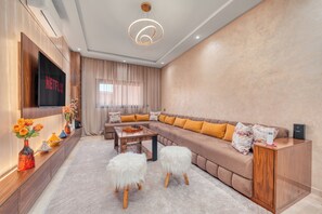Ein modernes Wohnzimmer mit einem großen Flachbildfernseher, einem Ecksofa, einem Holztisch und einer dekorativen Vase mit Blumen.