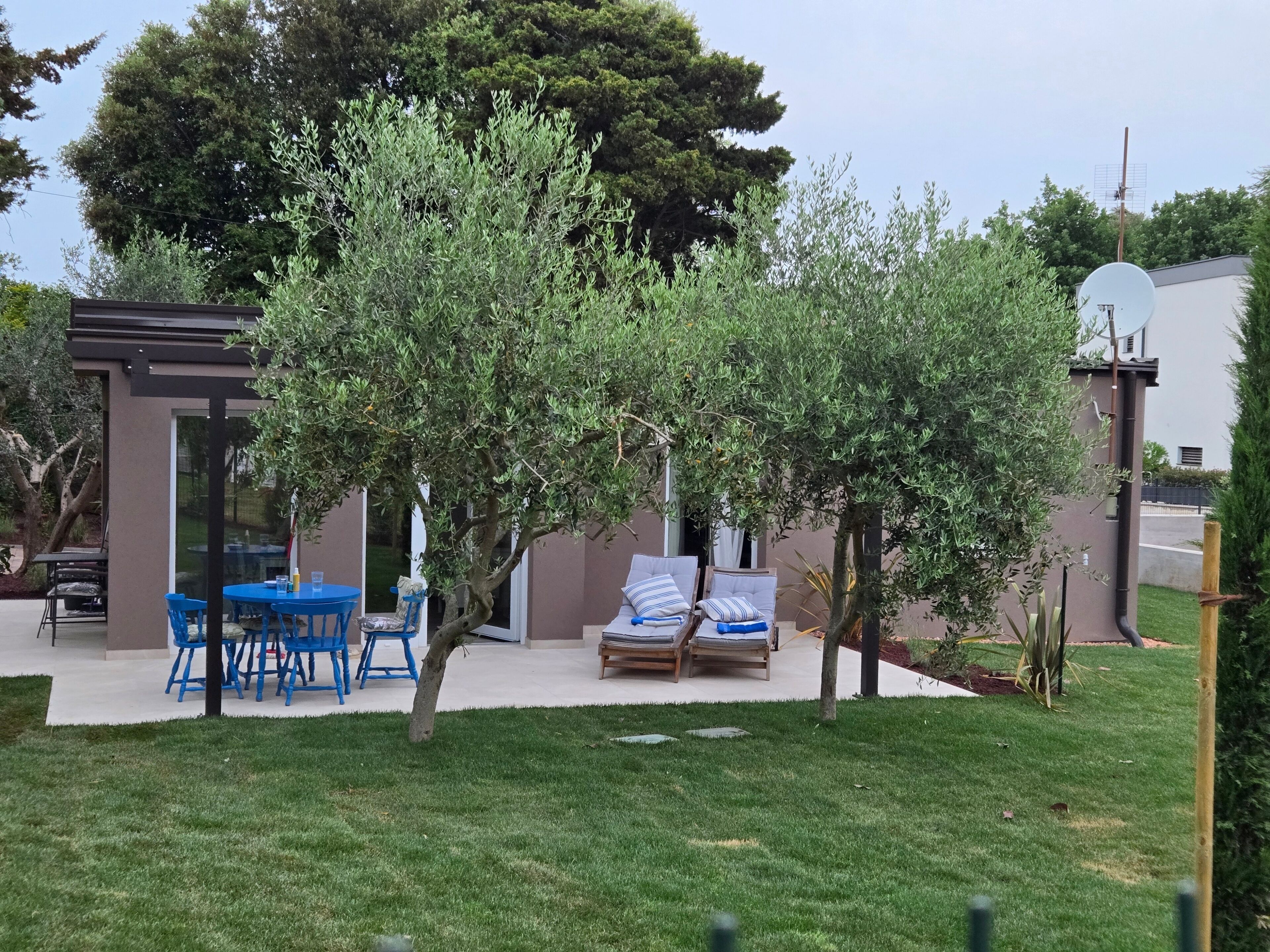 Eine Terrasse mit Tisch und Stühlen, ein kleiner Baum und ein Gebäude mit Satellitenschüssel.