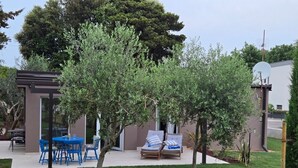 A patio area with a table and chairs, a small tree, and a building with a satellite dish. - Mediterranean oasis of peace- 100 m from the sea, private garden ful fenced yard (Banjole)