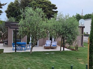 Eine Terrasse mit Tisch und Stühlen, ein kleiner Baum und ein Gebäude mit Satellitenschüssel.