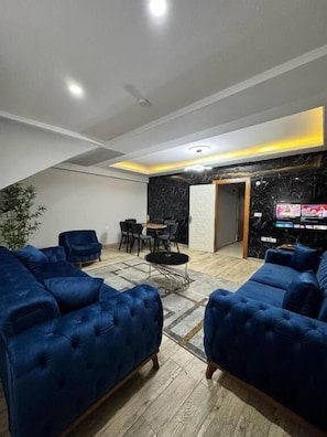 Uma sala de estar moderna com um sofá azul-escuro, uma mesa de jantar com cadeiras e uma TV de tela plana na parede.