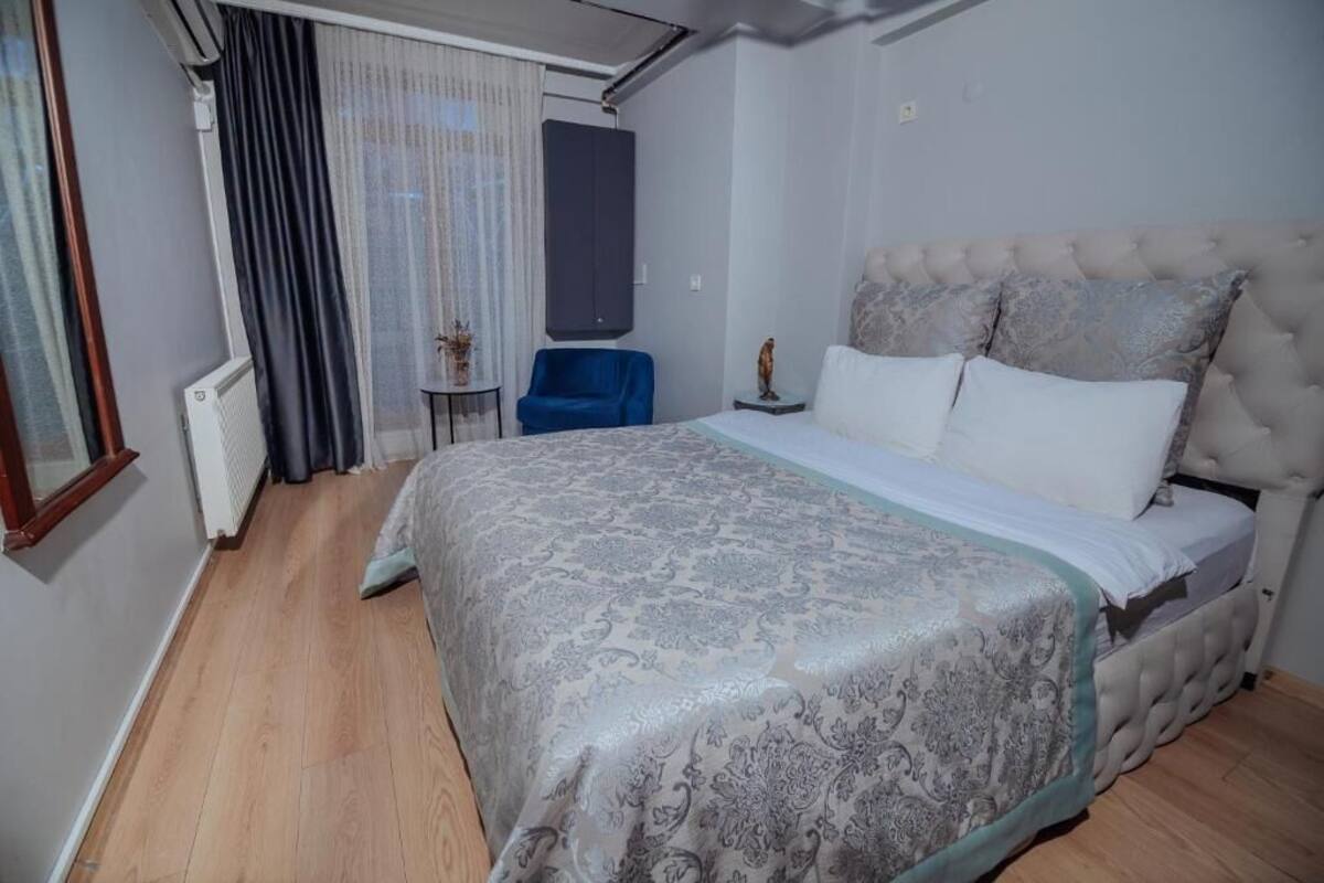 Ein Schlafzimmer mit einem Bett, einem Sessel, einem kleinen Tisch und einem Fenster mit Vorhängen.
