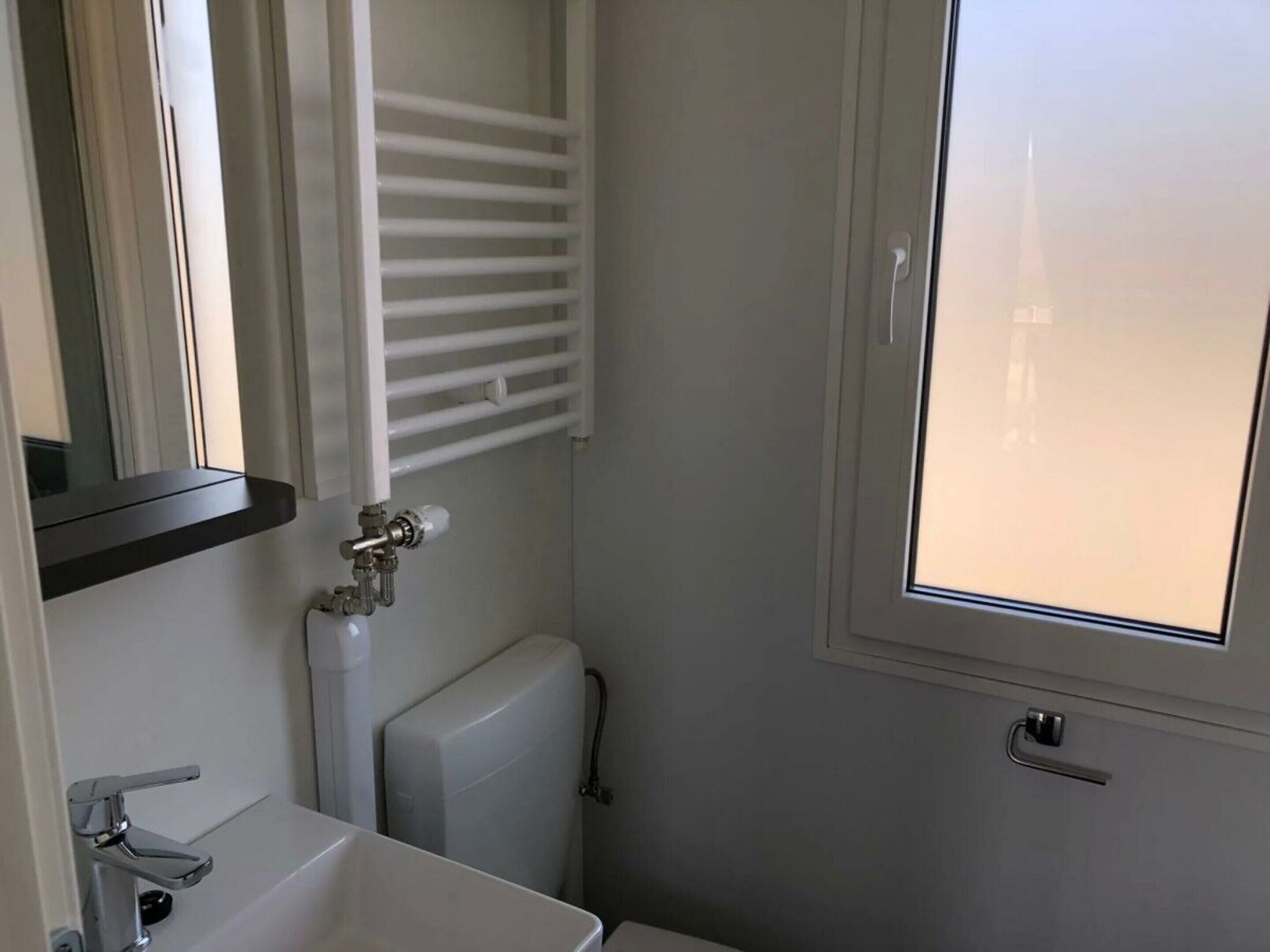 Un baño con inodoro, lavabo, radiador y ventana.