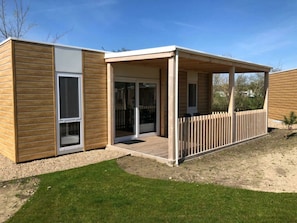 A modern building with a covered patio, large sliding glass doors, and a wooden fence. - Cosy Unique 2+4 (Nunspeet)