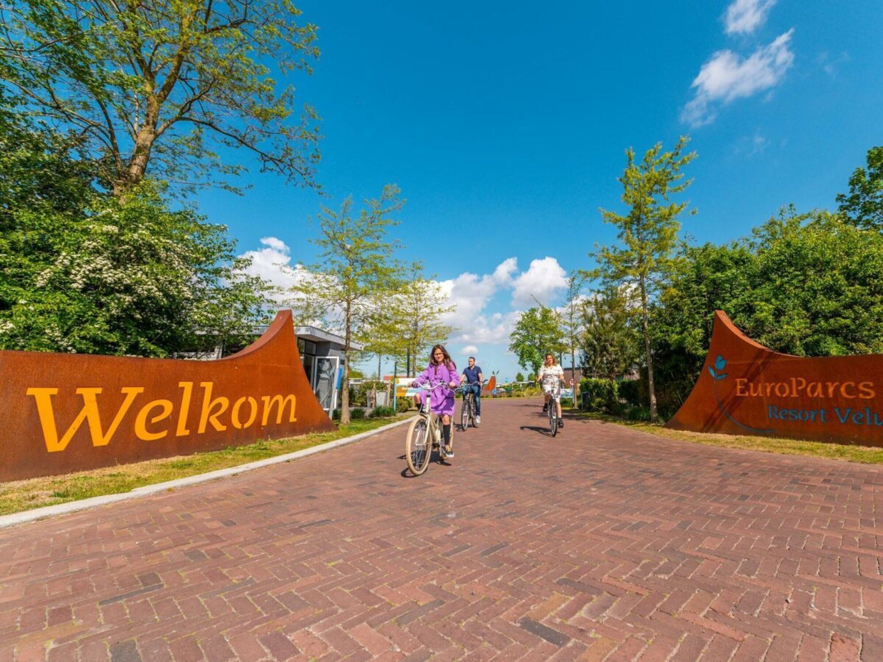 A brick pathway leading to a building with a 'Welcome' sign and a 'EuroParcs Resort Velu' sign.