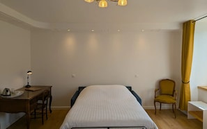 A room with a bed, a desk with a lamp, a chair, and a yellow curtain.