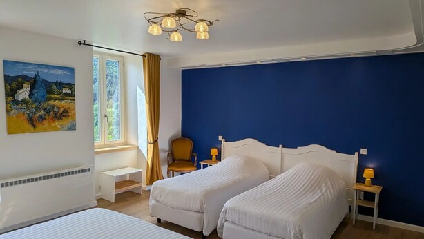 A bedroom with two beds, a window with curtains, a painting, and a unique ceiling light fixture. - Flexible & comfy guest room with mountain view (Montaillou)