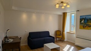A living room with a dark blue sofa, a small white table, a yellow armchair, a painting on the wall, and a window with curtains. - Flexible & comfy guest room with mountain view (Montaillou)