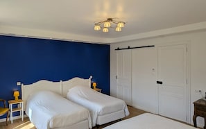 A bedroom with two beds, a blue wall, white doors, and a ceiling light fixture.