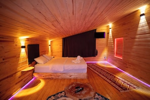 Habitación de cabaña de madera con una cama, luces fijadas a la pared y un control remoto sobre un tocón de árbol.