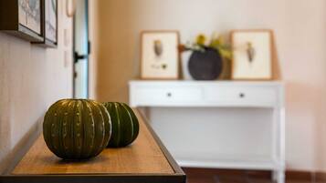 Un pasillo con un banco de madera, dos calabazas verdes, una consola blanca con marcos y un jarrón con flores.