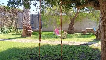 Une balançoire sous un arbre, dans un jardin avec un mur de pierres et une table de pique-nique en arrière-plan.