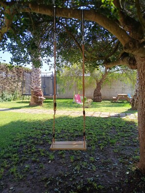 A swing set under a tree in a garden with a stone wall and a picnic table in the background. - 2-bedroom apartment in villa! (San Donato Di Lecce)