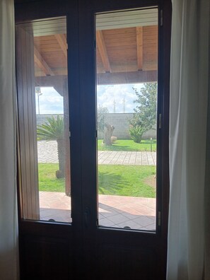 Vista attraverso una finestra, con travi in legno a soffitto e un muro in mattoni visibile all'esterno.