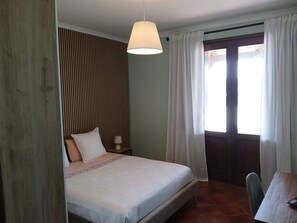 Una camera da letto con un letto, un comodino, una lampada, una finestra con tende e una porta.
