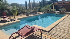 Piscina rectangular con terraza de madera y sillas de descanso.