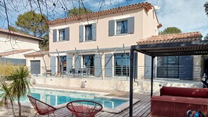 Una casa de dos pisos con piscina, mobiliario exterior y un patio cubierto.