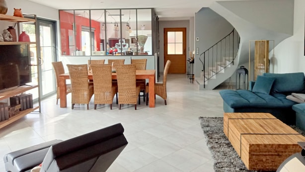 Una sala de estar moderna con un sofá, una mesa de centro, una zona de comedor con sillas y una escalera.
