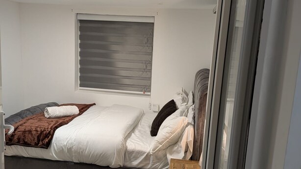 Ein Schlafzimmer mit Bett, Fenster mit Jalousien, einem Nachttisch und einem Beistelltisch.