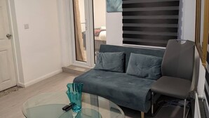 Ein Wohnzimmer mit Glastisch, grauem Sofa, einem Klavier und einer Glastür, die auf einen Balkon führt.