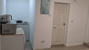 Eine kleine Küche mit Mikrowelle, Toaster und kleinem Herd. Eine weiße Tür mit Griff ist sichtbar, und ein Lichtschalter befindet sich an der Wand.