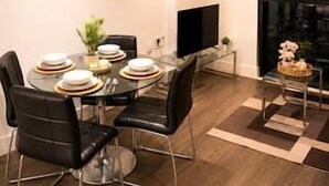 Un espace repas moderne avec une table en verre, des chaises noires et un téléviseur à écran plat.
