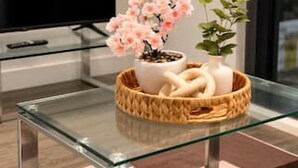 Un salon moderne avec une table basse en verre, un téléviseur et des objets décoratifs, notamment des fleurs et un vase.