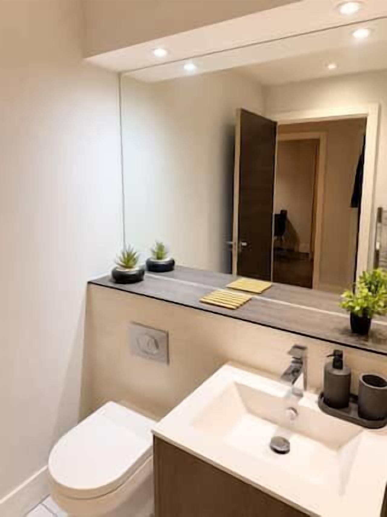 Une salle de bain moderne avec des toilettes blanches, un lavabo surmonté d’un miroir et un porte-serviettes.