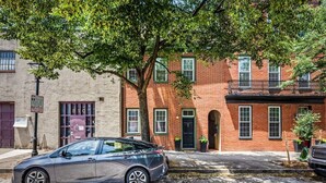 A two-story brick building with a car parked on the street in front. - Large home on a quiet street close to attractions (Baltimore)