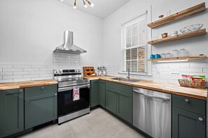 A modern kitchen with stainless steel appliances, green cabinets, and wooden countertops. - Large home on a quiet street close to attractions (Baltimore)