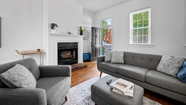 A modern living room with a fireplace, two grey sofas, a coffee table, and a view of the outside. - Large home on a quiet street close to attractions (Baltimore)