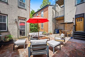 Eine Terrasse mit Gartenmöbeln, einem roten Sonnenschirm und einem Pflasterboden.