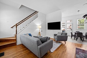 Ein modernes Wohnzimmer mit Treppe, grauen Sofas, einem Flachbildfernseher und einem Essbereich.